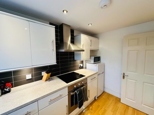 Modern kitchen with white cabinets, stainless steel appliances, and wooden flooring.