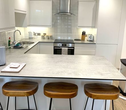 Modern kitchen with a stone countertop and three wooden bar stools.